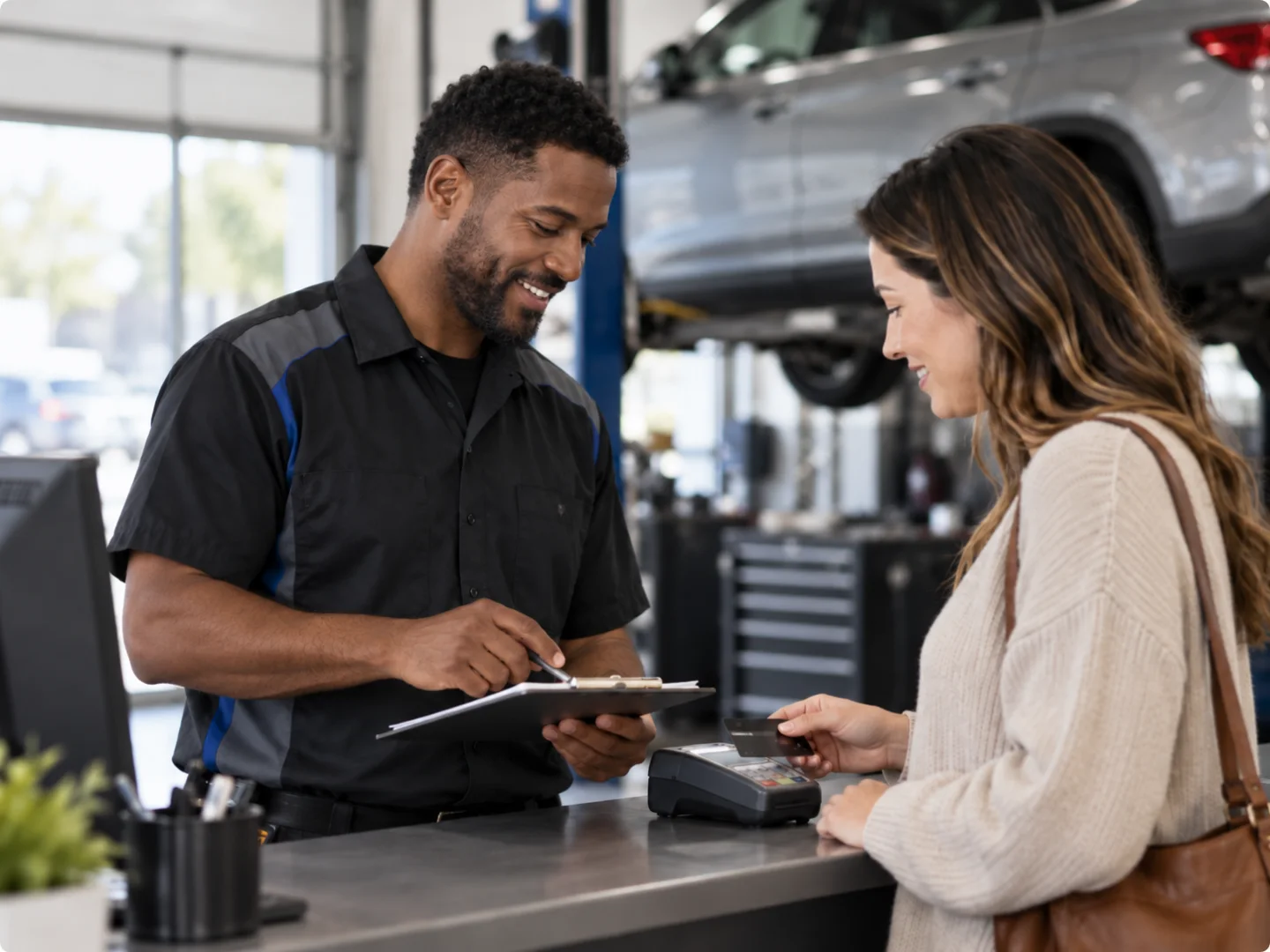 Auto service professional reviewing a repair order while a customer prepares a card payment