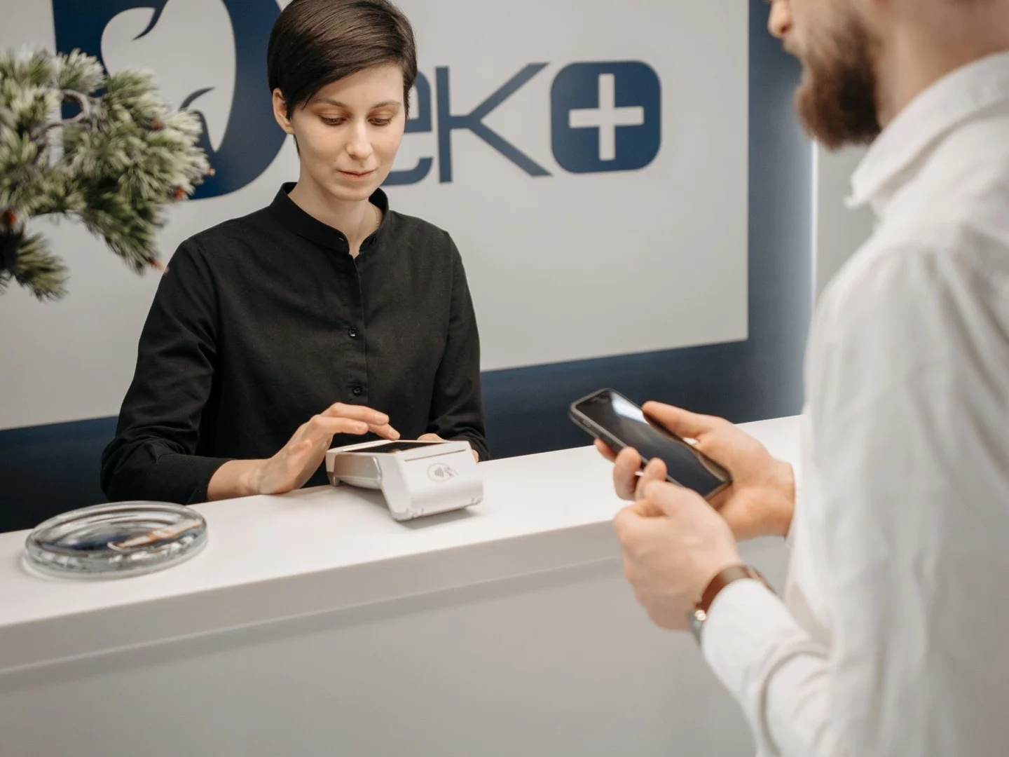 Patient completing a contactless payment with a receptionist at a modern clinic front desk