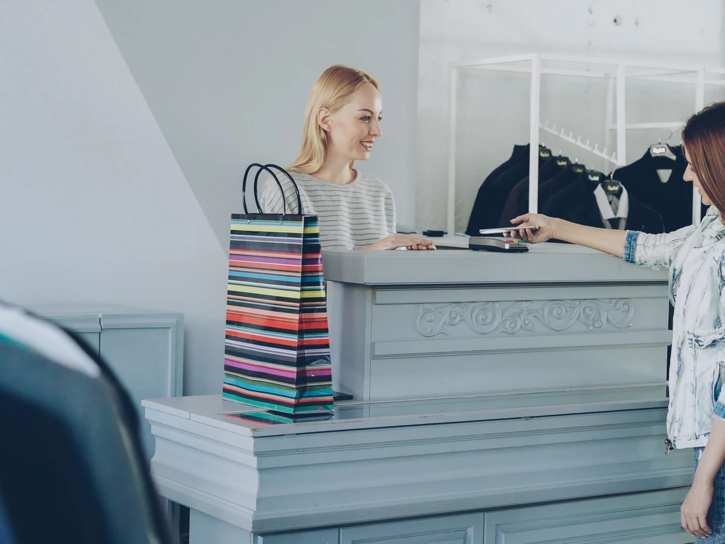Boutique customer tapping a phone on a countertop payment terminal at checkout